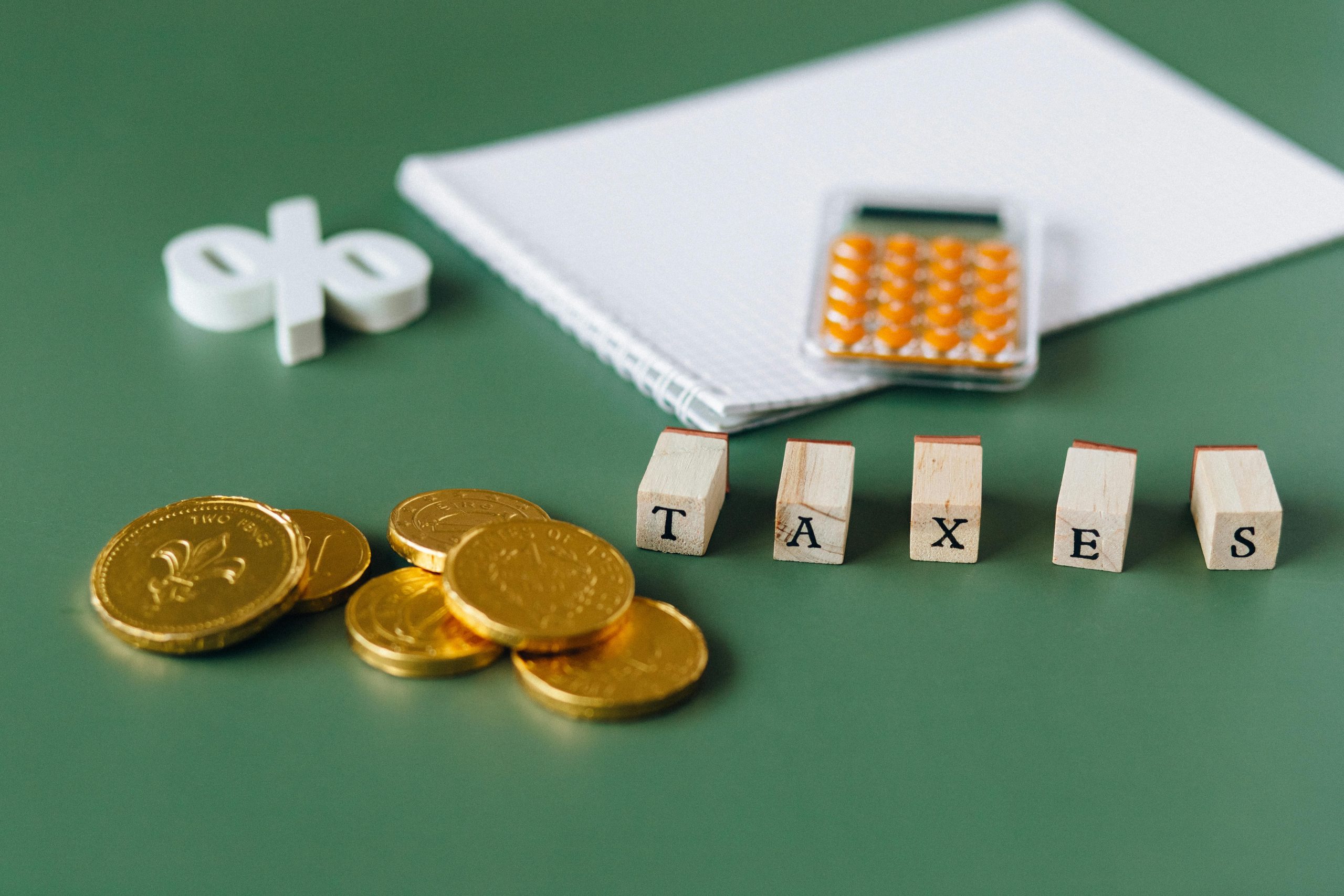 Close-up of tax-related items including coins, calculator, and word 'taxes' on a green background.